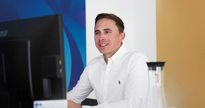 Fabian Kampfmann, Head of Sales – Key Account Management bei PropertyExpert, sitzt lächelnd vor einem Bildschirm.
