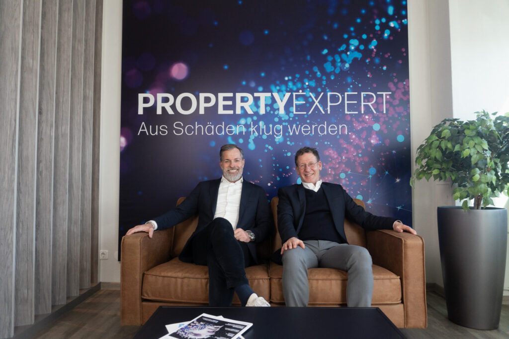 Die Geschäftsführer Frank Feist und Wolfgang Kallweit vor der Logowand im Empfangsbereich von PropertyExpert