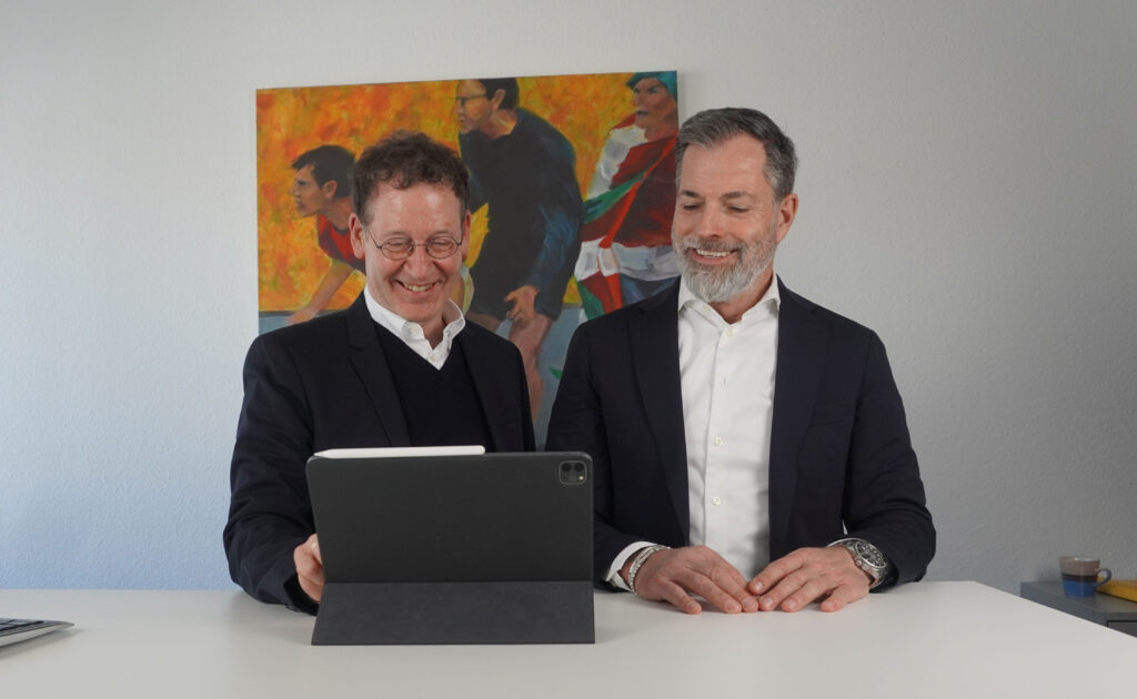Die Geschäftsführer Wolfgang Kallweit und Frank Feist von PropertyExpert lächelnd im Büro auf ein Tablet schauend.