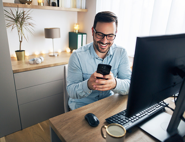 Lächelnder Mann am Schreibtisch mit einem Smartphone in der Hand.